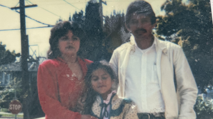 A Latina mom wearing a red suit dress, a young girl, and her father stand in a photo outdoors